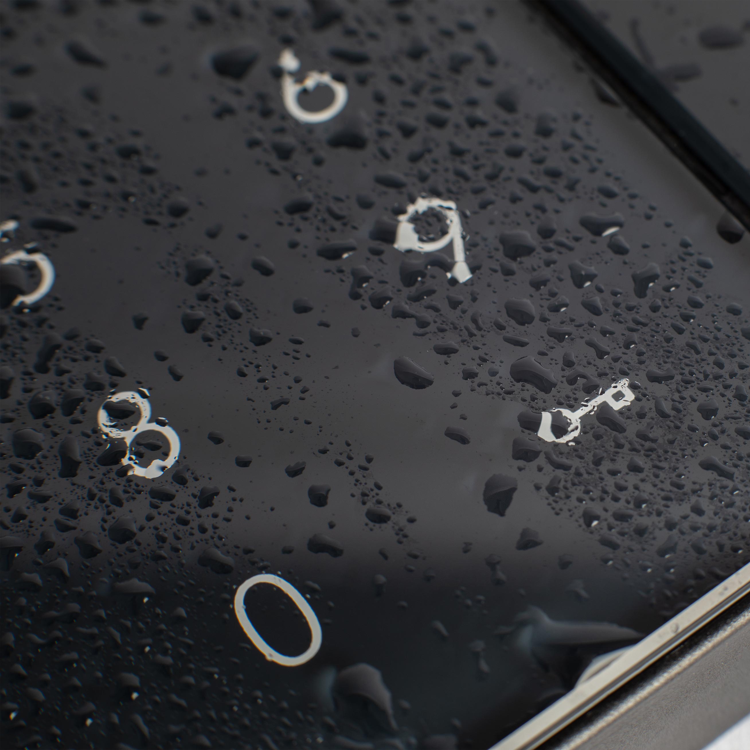 Nahaufnahme einer schwarzen Tastatur mit weißen Buchstaben und Wassertropfen auf den Tasten